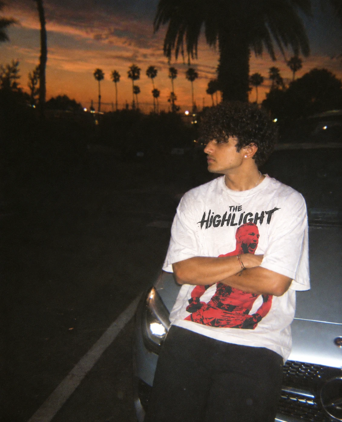 Fan in a white The Highlight tee at dusk under palm trees